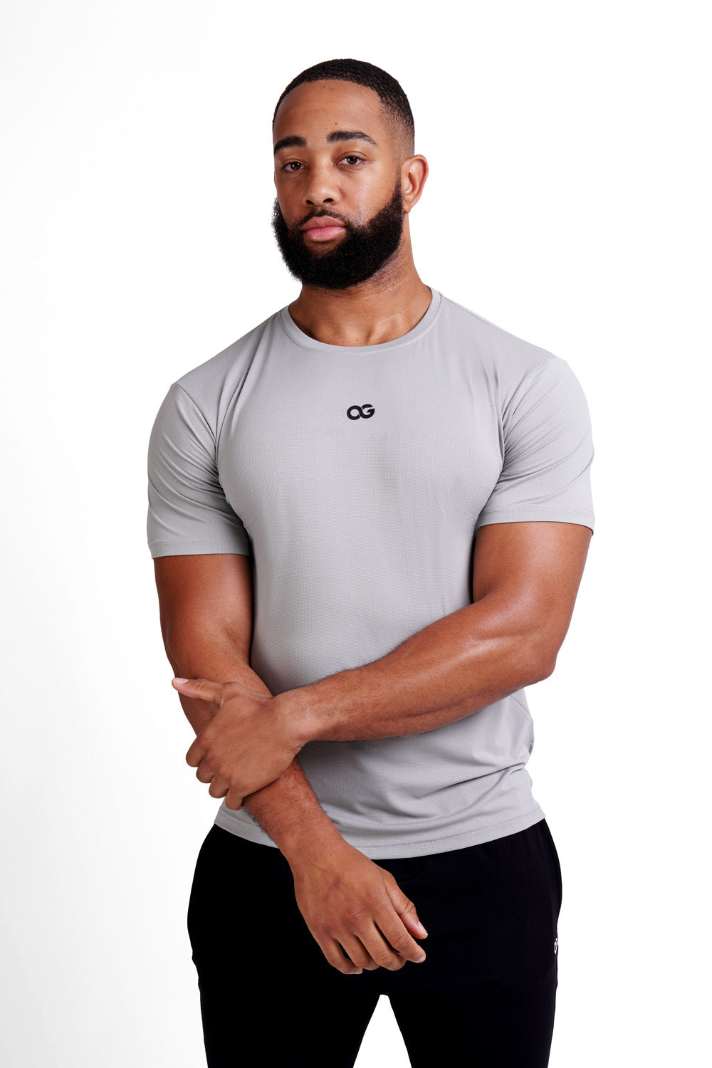 OG Men's Premium Performance Tee Grey - Front view, arms crossed, black OG logo on chest - Original Greatness